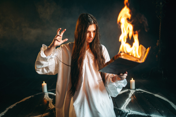 Witch in white shirt  reading spell, pentagram circle with candles, dark magic ritual. Occultism and exorcism - 写真・画像