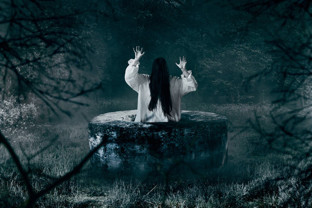 Witch in white shirt gets out of an abandoned well in the night. Dark magic, occultism and exorcism, witchcraft - Photo, Image