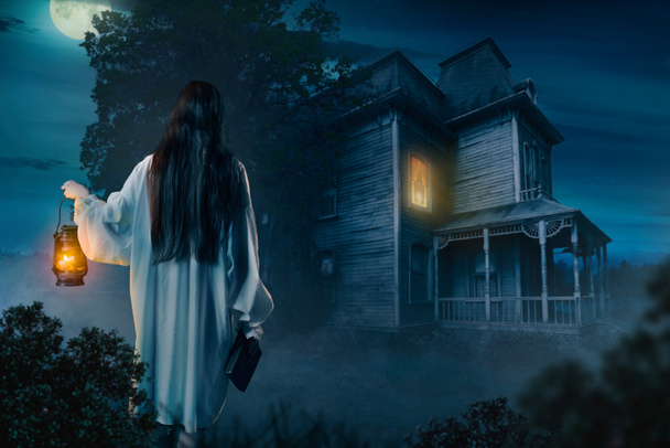 jeune femme avec lampe au kérosène et livre d'sorts contre maison abandonnée la nuit
 - Photo, image