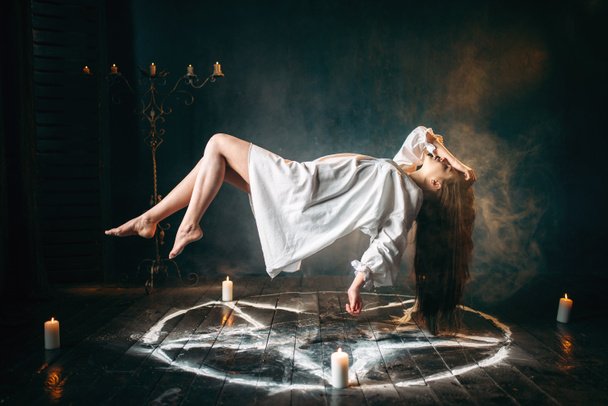 молодая женщина в белой рубашке пролетает над кругом пентаграммы, волшебство гарка, ритуал жертвоприношения. Оккультизм и экзорцизм
 - Фото, изображение