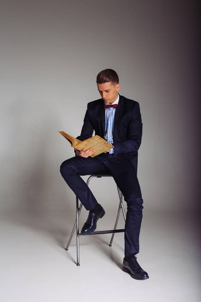 a man, a guy in a blue suit, sits on a chair and reads an old book, the concept of knowledge, study, science, business, everything new, it's a well-forgotten old - Photo, Image