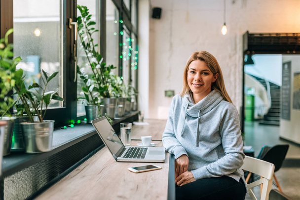 Portrait of a beautiful woman in casual clothing sitting at the cafe in front of laptop. Looking at camera. - Photo, Image