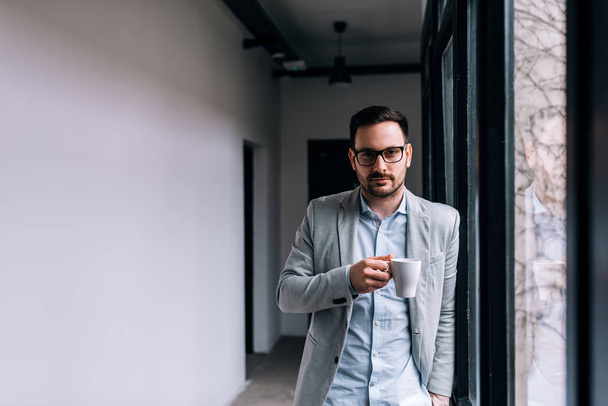 Portrait of a handsome man holding a mug in the hallway near the window. Looking at camera. - Foto, imagen