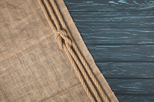 top view of knotted brown nautical rope on sackcloth on wooden background - Fotografie, Obrázek