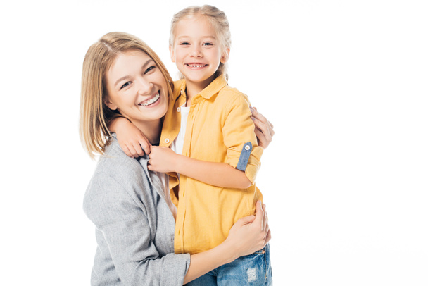 Porträt einer glücklichen Mutter und einer niedlichen Tochter, die in die Kamera schauen, während sie sich isoliert in Weiß umarmen - Foto, Bild