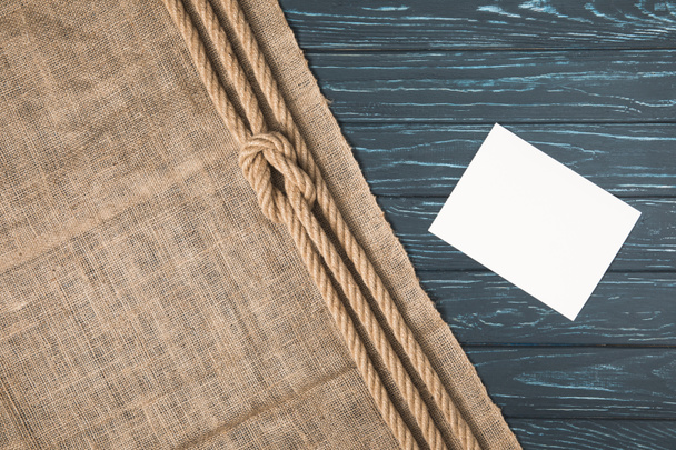 Geknoopte bruin nautische touw op zak en lege papier op een houten oppervlak (bovenaanzicht) - Foto, afbeelding