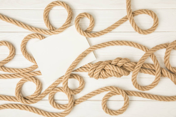 top view of empty paper on brown nautical knotted ropes on white wooden surface - Photo, Image