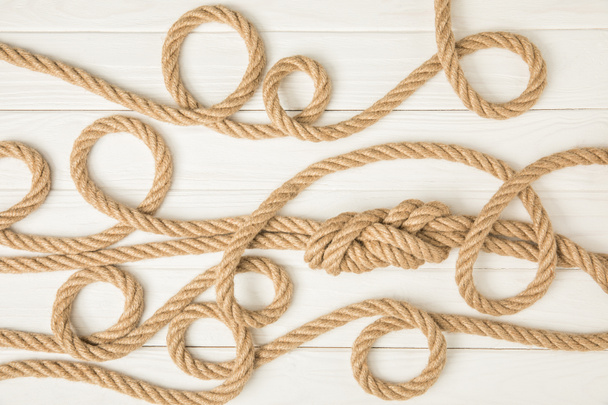top view of brown nautical knotted ropes on white wooden surface - Фото, зображення