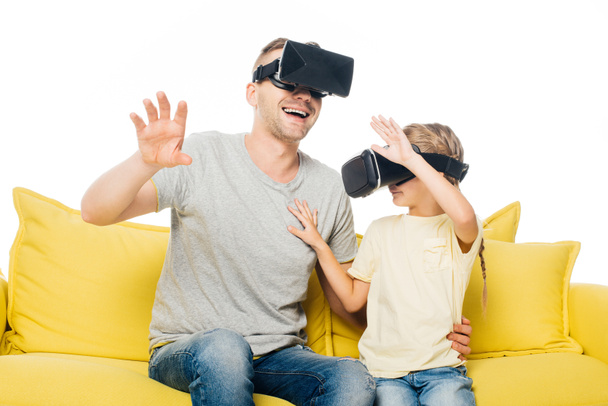 father and daughter in virtual reality headsets on yellow sofa isolated on white - Foto, Imagem