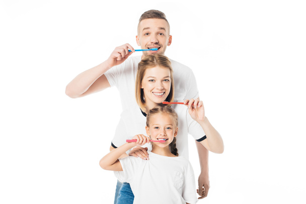 Porträt einer lächelnden Familie in ähnlicher Kleidung mit Zahnbürsten isoliert auf weiß - Foto, Bild