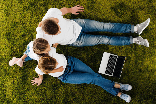overhead view of family with laptop resting on green lawn - Photo, Image