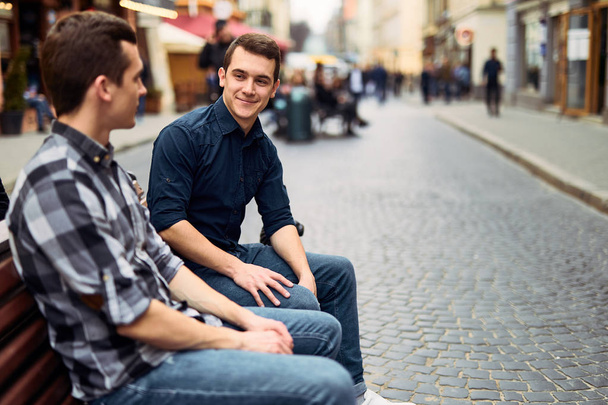 Two man sit on bench and talk on the street  - Fotó, kép