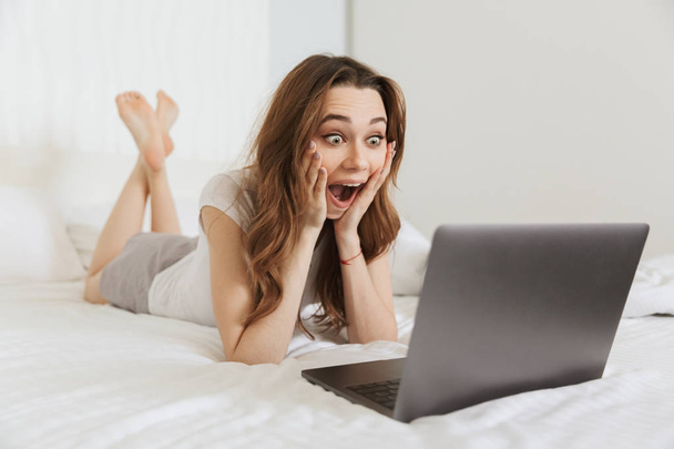 Portrait of an excited young woman lying in bed at home - Foto, afbeelding
