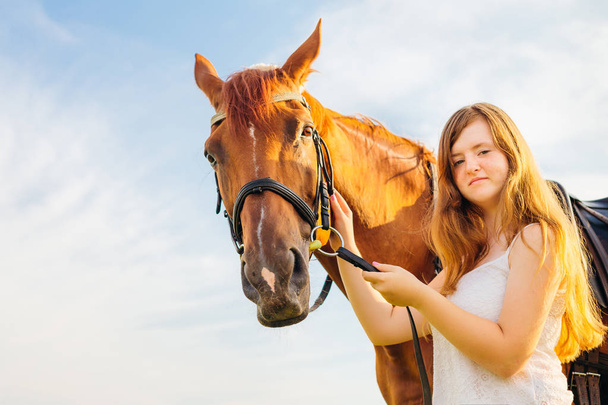 A pretty girl holds a horse for a bridle and they look in the camera lens - Zdjęcie, obraz