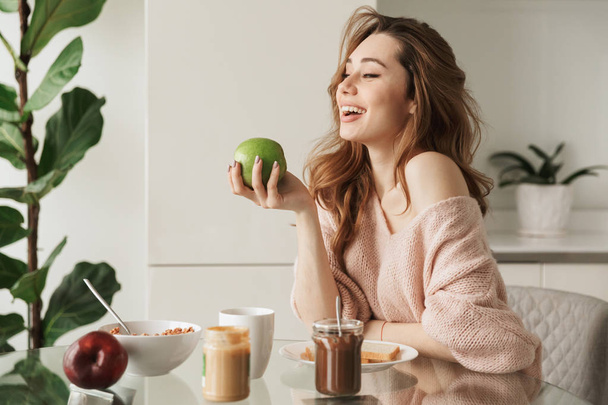 Portrait of a laughing young woman having tasty breakfast - Фото, изображение