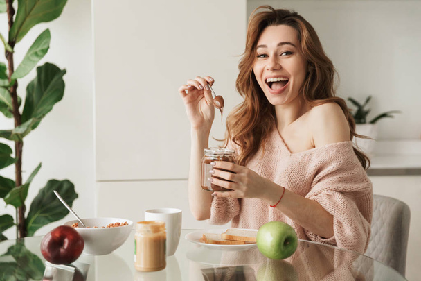 Portret van een vrolijke jonge vrouw lekker ontbijten - Foto, afbeelding