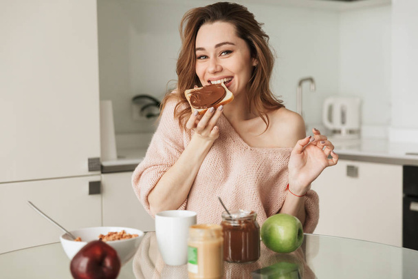 Portrait of a happy young woman having tasty breakfast - Фото, изображение