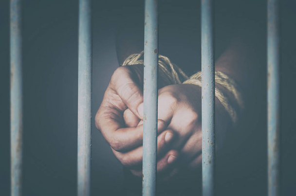 Руки в'язня пов'язані мотузкою за металевими в'язницями
 - Фото, зображення
