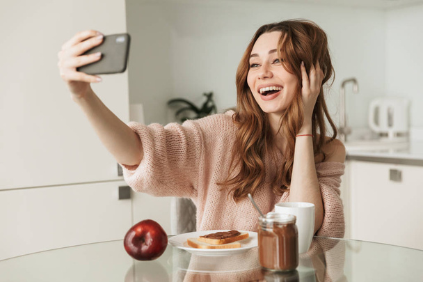 Portrait of a smiling young woman taking a selfie - Фото, изображение