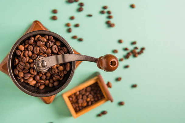 Coffee beans in a hand-held coffee grinder on a tender green bac - Fotó, kép