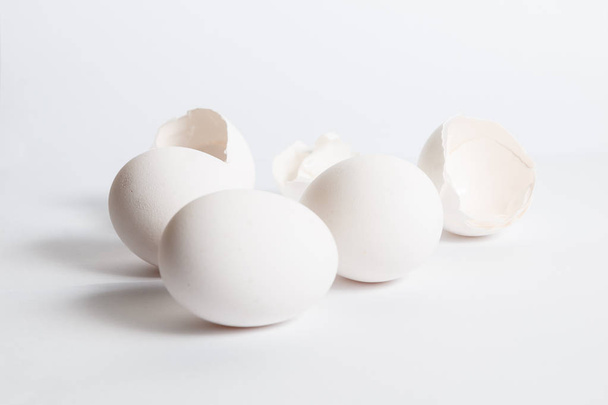 Huevos blancos distribuidos en superficie blanca. Sombra lateral suave. Cáscaras de huevo rotas
. - Foto, imagen