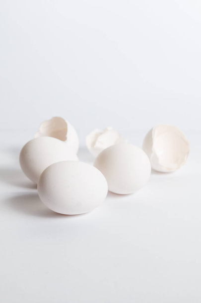 White eggs distributed on white surface. Soft side shade. Broken egg shells. - Фото, изображение