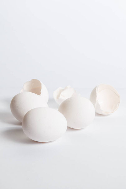 weiße Eier auf weißer Oberfläche verteilt. weicher Seitenschatten. Zerbrochene Eierschalen. - Foto, Bild
