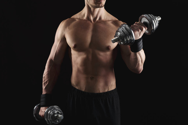Сильный спортсмен с гантелями демонстрирует обнаженное мускулистое тело
 - Фото, изображение