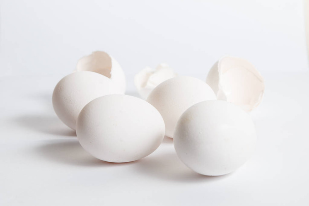 Uova bianche distribuite su superficie bianca. Ombra laterale morbida. Gusci d'uovo rotti
. - Foto, immagini