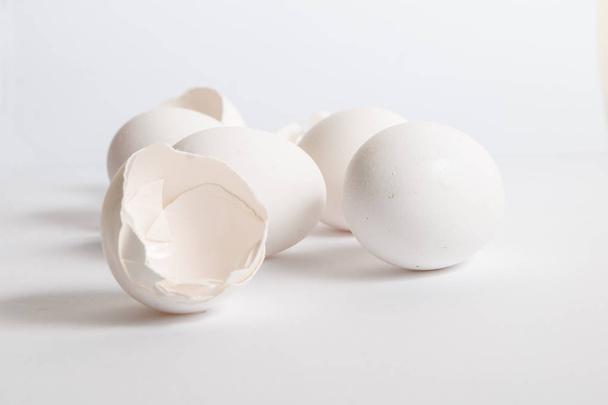 Beyaz yumurta beyaz yüzey üzerinde dağıtılmış. Yumuşak yan gölge. Kırık yumurta kabukları. - Fotoğraf, Görsel