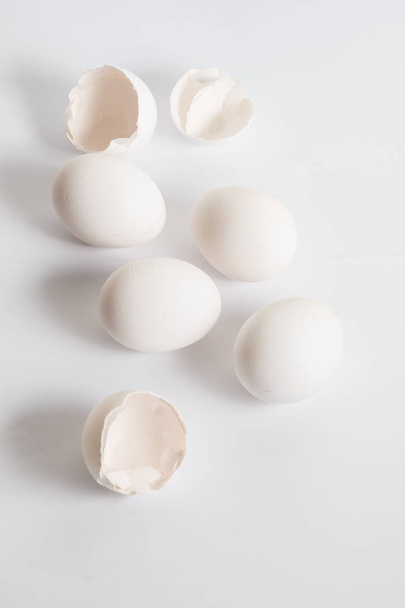 Beyaz yumurta beyaz yüzey üzerinde dağıtılmış. Yumuşak yan gölge. Kırık yumurta kabukları. - Fotoğraf, Görsel