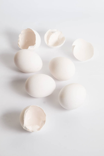 weiße Eier auf weißer Oberfläche verteilt. weicher Seitenschatten. Zerbrochene Eierschalen. - Foto, Bild