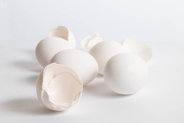 Άσπρα αυγά διανέμονται σε λευκή επιφάνεια. Μαλακή πλευρά σκιά. Σπασμένο αυγό κοχύλια. - Φωτογραφία, εικόνα