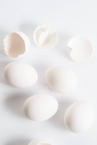 Huevos blancos distribuidos en superficie blanca. Sombra lateral suave. Cáscaras de huevo rotas
. - Foto, imagen
