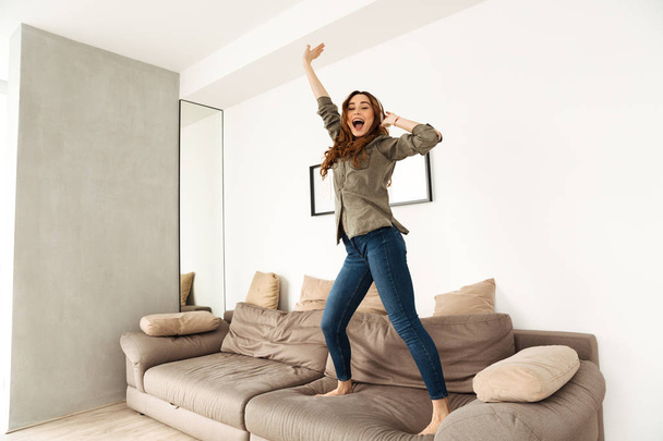 Image of cheerful woman 20s in casual clothing dancing on couch  - Foto, Imagem