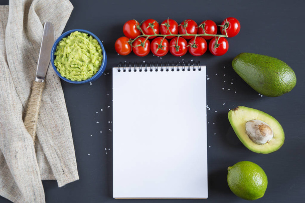 Traditional latinamerican mexican sauce guacamole in ceramic bowl and ingredients on dark background. Notebook. Top view. Flat lay. Copy space. - Photo, Image