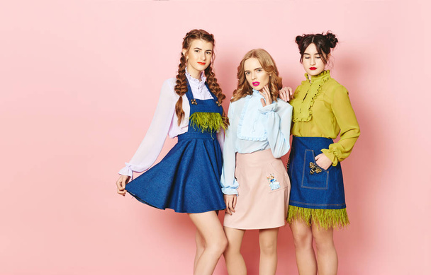 Mode foto van drie jonge meisje poseren op roze achtergrond in de studio - Foto, afbeelding