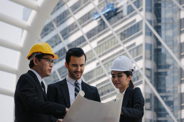 group of business or engineer woman and man with safety helmet and blueprint planning at the building and checking their work in modern city, planning start up new project, successful concept - 写真・画像
