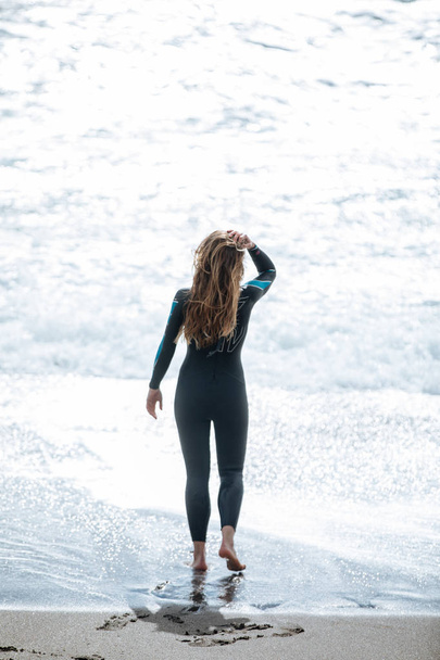Młoda kobieta, rozciąganie przed pływać na sobie kombinezon na morzu - Zdjęcie, obraz