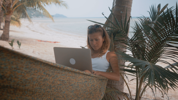 Žena na volné noze pracuje na pláži v houpací síti - Záběry, video