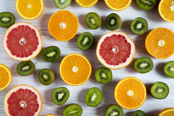Byt leží. Pohled shora. Krájené tropické ovoce: kiwi, pomeranče, grapefruitu a mandarinky na světlé dřevěné pozadí. Letní pozadí - Fotografie, Obrázek