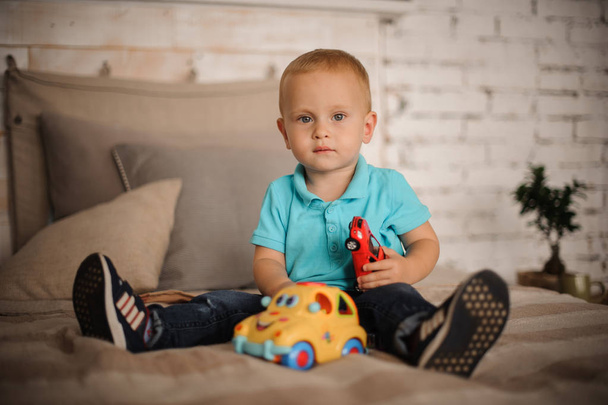Cute little boy sitting on the bed with a car toy - Fotografie, Obrázek