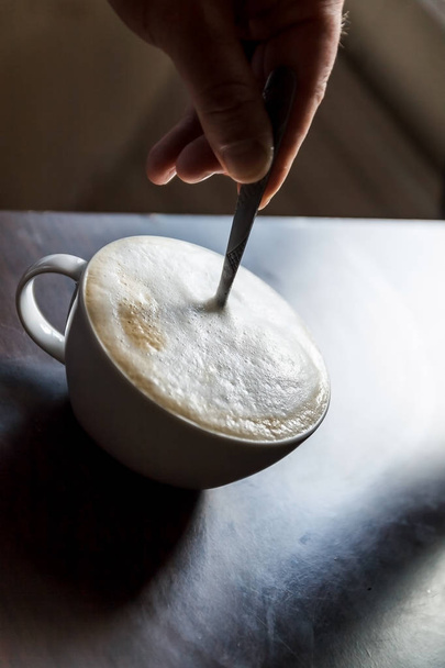Filiżanka kawy z pianką miesza się przez ludzką ręką - Zdjęcie, obraz