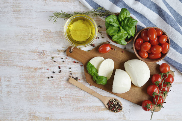 Ser mozzarella, czerwone pomidory i liści bazylii, pieprz, oliwa z oliwek, drewniane biurko, zdrowe jedzenie koncepcja - Zdjęcie, obraz