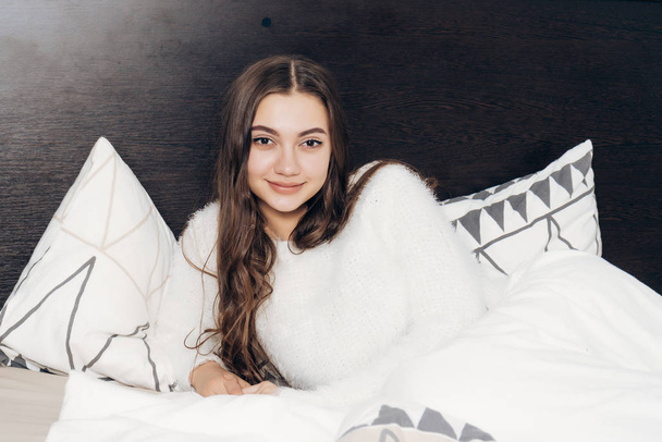 lovely long-haired girl is lying in bed, woke up early in the morning and smiles - Fotó, kép