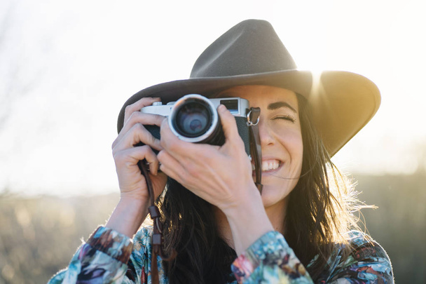 Uśmiechnięta młoda kobieta używa aparatu fotograficznego do robienia zdjęć. - Zdjęcie, obraz