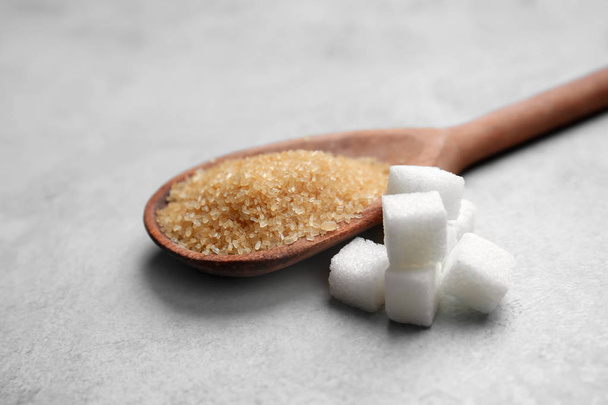 Εκλεπτυσμένη κύβους και καστανή ζάχαρη σε κουτάλι σε γκρίζο φόντο - Φωτογραφία, εικόνα