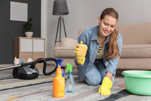 Young woman cleaning carpet at home - Foto, afbeelding