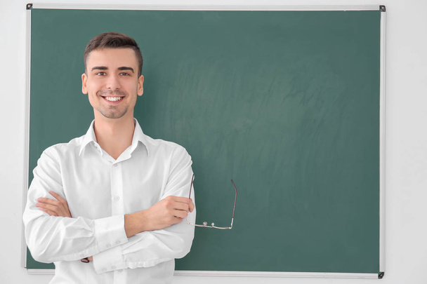 Young male teacher standing near blackboard on white background - Photo, Image