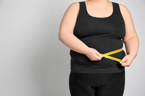 Overweight woman with measuring tape on light background - Foto, immagini